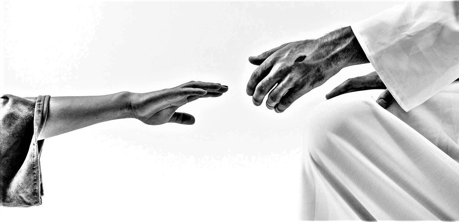 a hand reaching out to hold the nail pierced hand of Jesus