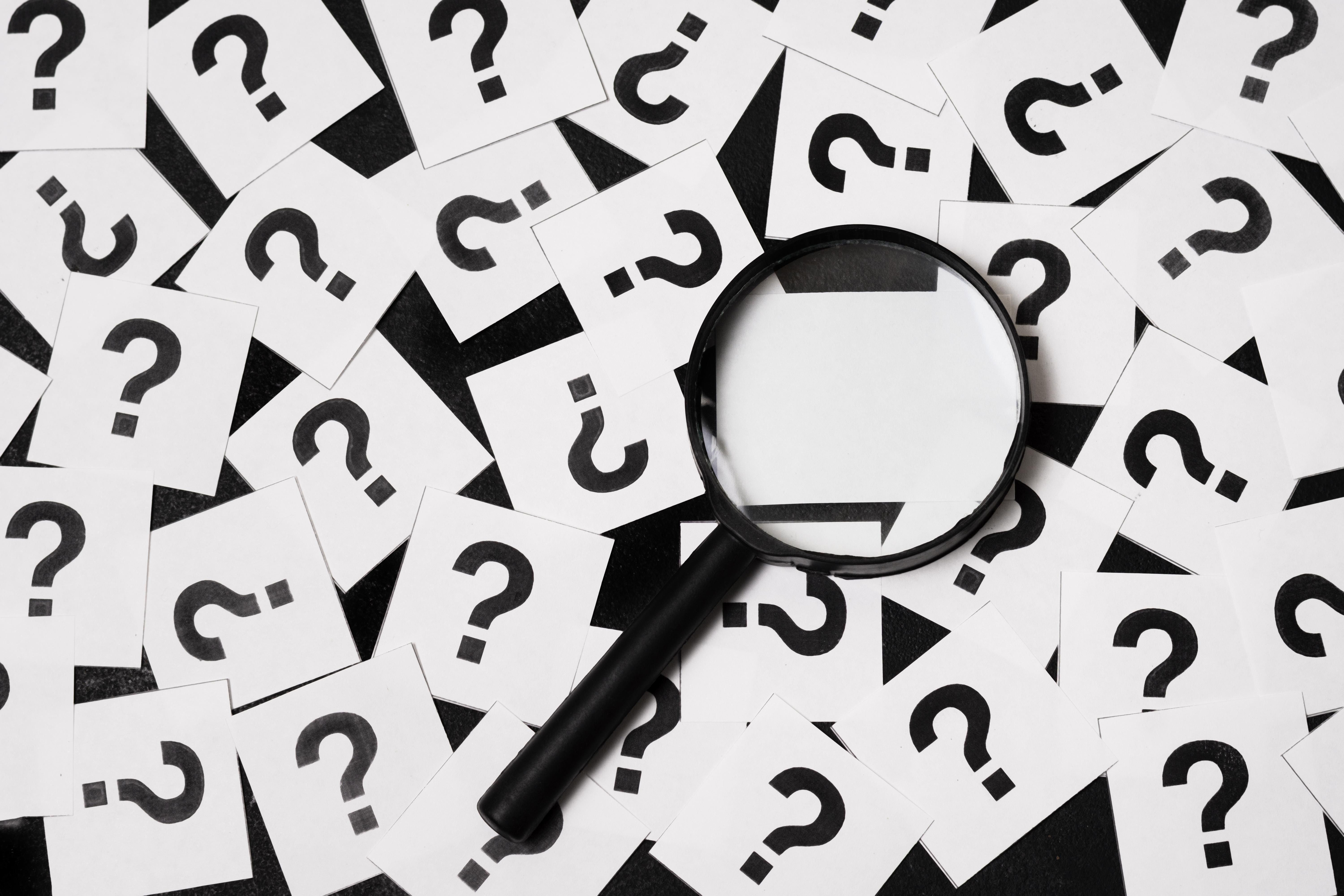 a black magnifying glass on top of a pile of white cards with question marks on them.